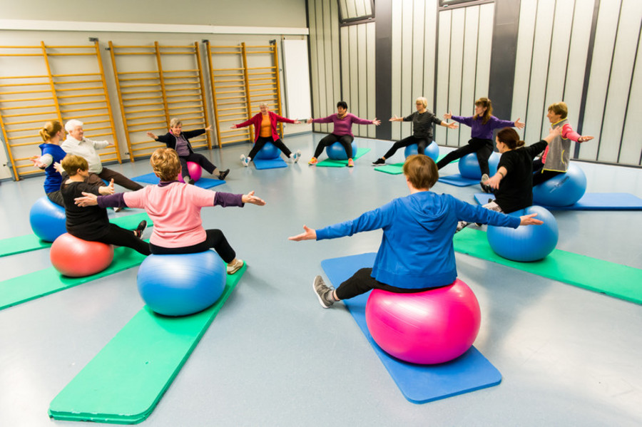 gruppe sitzt auf großen Gymnastikbällen im Kreis und schwingen die Arme