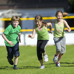 Drei Kinder rennen über eine Wiese.